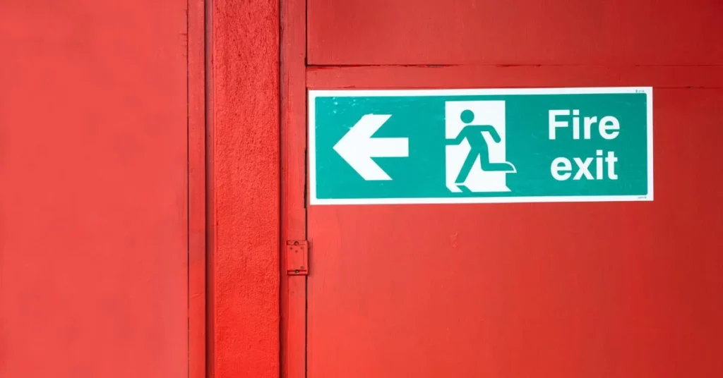 White and green 'fire exit' sign with running man symbol and arrow, on a red wall.